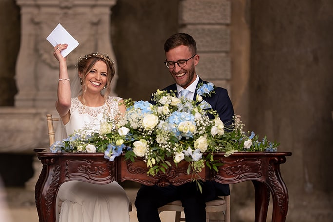Married couple sitting with bride Ellen happily waving wedding certificate